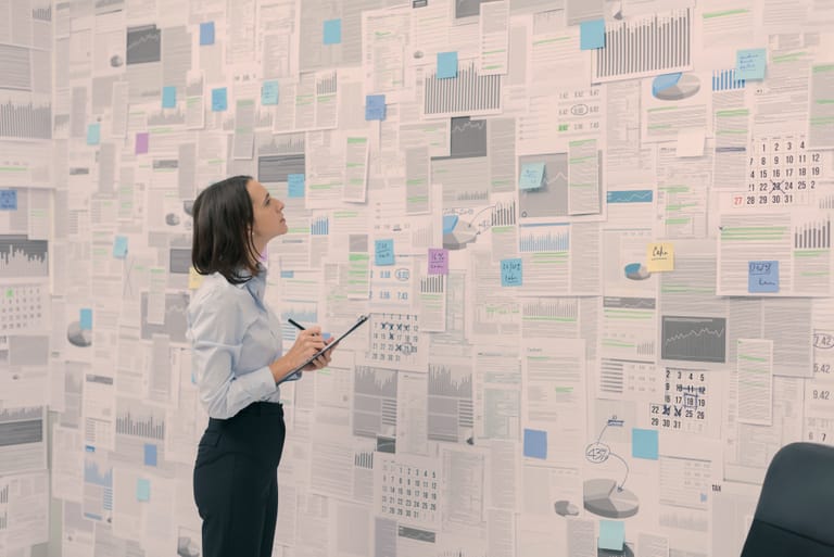 Corporate businesswoman checking financial data and reports hanging on a wall, management and strategy concept